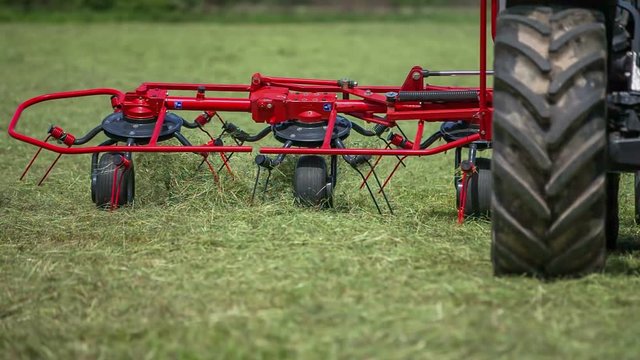 Agricultural machinery with rotary rakes is moving very fast when a farmer is preparing hay on a large field.
