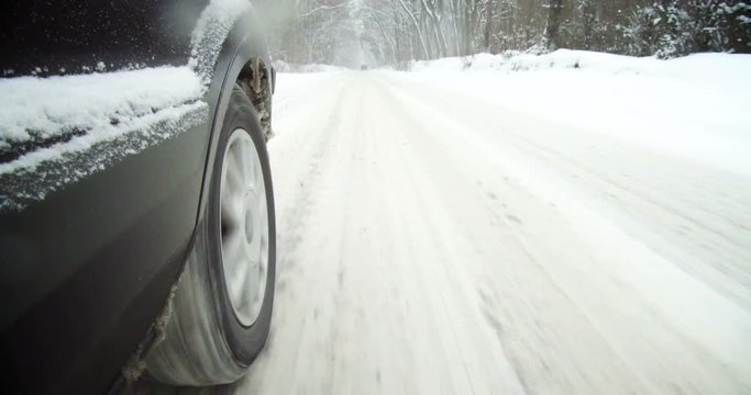 Color footage of a car driving on a snowy road, with close up on the wheel.