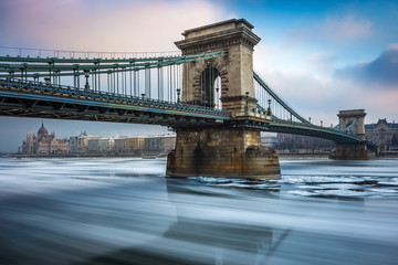 Obraz premium Budapest, Hungary - The famous Szechenyi Chain Bridge on the icy River Danube on a cold winter morning with Hungarian Parliament at the background