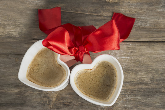 valentine's day/two cups of coffee heart shape with scarlet ribbon on old wooden background top view
