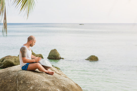 Man is sitting on the stone and playing hangdrum