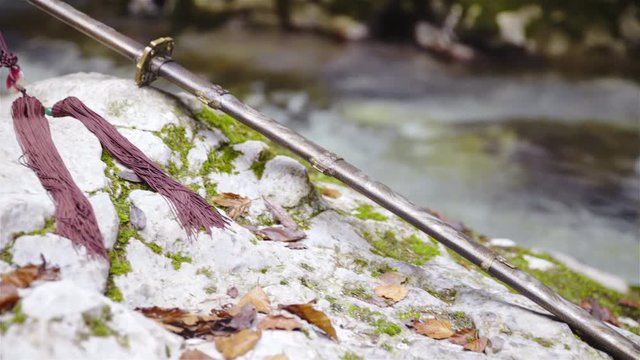 Medieval sword lying on rock by the river panning over 4K
