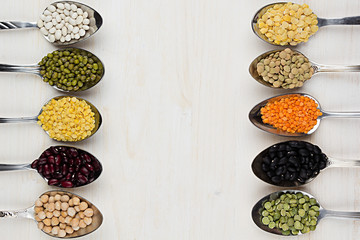Decorative border of assortment different beans in  spoons with copy space on white wood background. Top view, closeup.