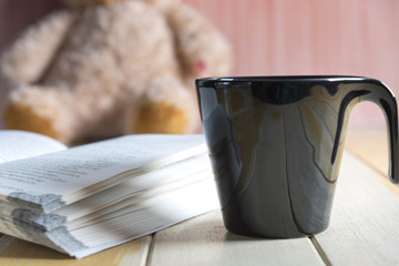 coffee cup and book focused on teddy bear in Blurred background