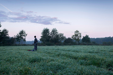 Man standing with stool and backpack in meadow at dawn. Noordijk