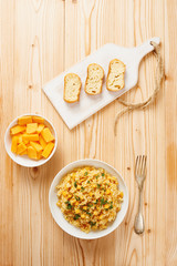 Pumpkin risotto on white dish, slices of bread on chopping board and raw pumpkin slices on white bowl