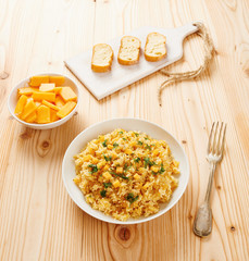 Pumpkin risotto on white dish, slices of bread on chopping board and raw pumpkin slices on white bowl
