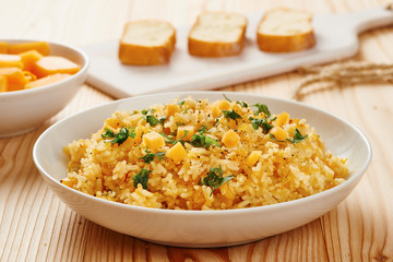 Pumpkin risotto on white dish, slices of bread on chopping board in the background