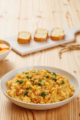 Pumpkin risotto on white dish, slices of bread on chopping board in the background