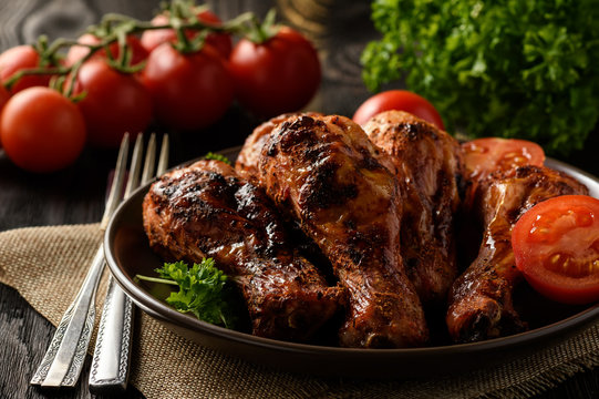 Roasted chicken legs with tomatoes on wooden background.