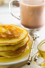Glass mug with cocoa, silver spoon, honey and pancakes