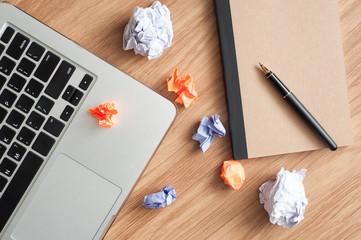 laptop computer, crumpled paper, pen and notebook on the wooden desk