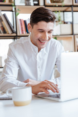 Laughing man dressed in white shirt using laptop