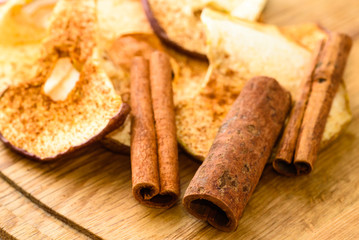 Whole cinnamon and dehydrated apple slices with powdered cinnamon on wooden cutting board.