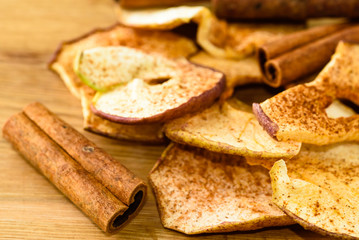 Whole cinnamon and dehydrated apple slices with powdered cinnamon on wooden cutting board.