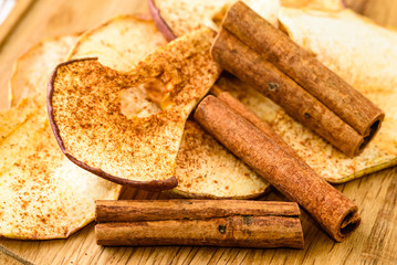 Whole cinnamon and dehydrated apple slices with powdered cinnamon on wooden cutting board.