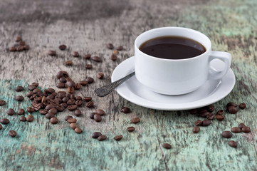 A cup of black coffee on the wooden table with coffee beans are scattered. Black coffee hot drink Grains Newspaper Wooden background White cup Breakfast