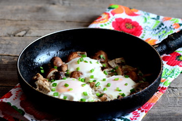 Delicious fried eggs with chopped mushrooms and fresh green onions in pan. Vegetarian egg recipe. Breakfast or lunch idea. Old wooden background. Rustic style. Closeup