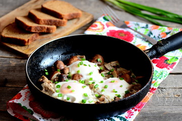 Fried eggs in pan. Organic eggs fried with mushrooms and green onions. Brown bread slices, fork, fresh green onions on a wooden table. Healthy egg recipe. Rustic style. Closeup