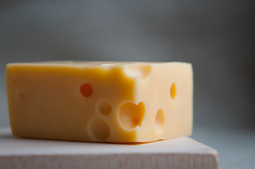 A triangle piece of maasdam cheese with holes served in rustic style on a wooden board. Close up. Eco food, meal, lunch concept