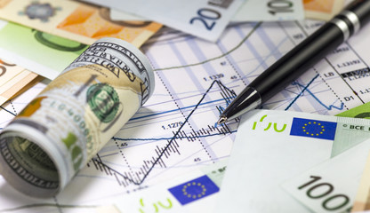 Us dollar bill and euro bills lying on the chart of dollar euro prices.Japanese candlesticks on the diagram. Pen on the graph. Concept of currencies trading. Selective shallow focus.
