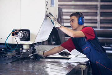 Inside a factory, industrial worker in action on metal press machine holding a steel piece ready to...