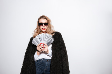 Beautiful young woman in fur coat holding US dollar bills