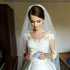 Thughtful bride holds blue boutonniere in her arms