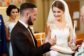 Pretty bride smiles sincerely while groom puts wedding ring on h