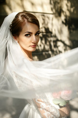 Naklejka premium Wind blows away bride's veil while she poses in trees' shadows