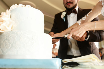 Bride and groom cut blue wedding cake on glass table with white