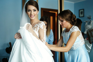Pretty bride smiles while bridesmaid laces up her corset