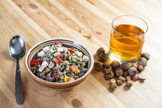 Traditional ukrainian cereal wheat porridge with raisins, nuts, poppy seeds, honey and candied fruit in earthenware bowl with dried fruit drink on natural wood table
