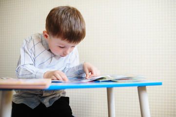 little boy is sitting at his desk and reads a book