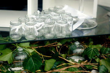 Glass bottles with white ribbons stand on table over greenery