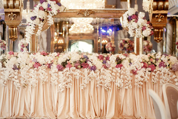 Long dinner table covered with beige cloth and decorated with fl