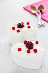 Valentine day decoration, breakfast, yogurt with berries for two in white heart-shaped bowls on the table.
