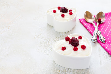 Valentine day decoration, breakfast, yogurt with berries for two in white heart-shaped bowls on the table.