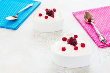 Valentine day decoration, breakfast, yogurt with berries for two in white heart-shaped bowls on the table.