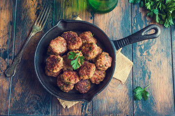 Homemade roasted beef meatballs in cast-iron skillet on wooden table in kitchen, fresh parsley, vintage fork, top view. - 133092790