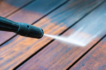 cleaning terrace with a power washer - high water pressure cleaner on wooden terrace surface - focus on the end of washer - shallow depth of field