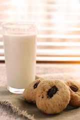 Glass transparent cup with milk and chocolate chip cookies standing at the window.