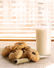 Glass transparent cup with milk and chocolate chip cookies standing at the window.