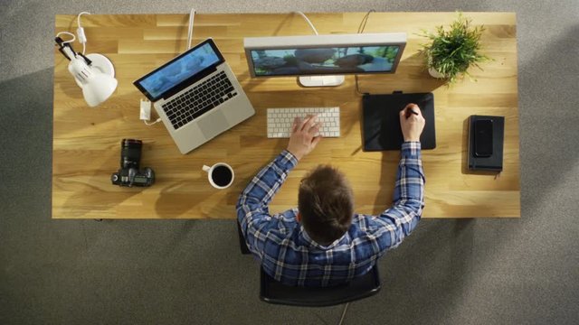 Top View of Young Talented Photographer Working on Digital Drawing Tablet at His Desktop Computer. Processing Wedding Photography. His Workplace is Covered with Sunlight.