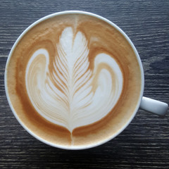 Top view of a mug of latte art coffee on timber background.