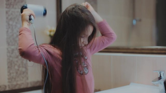 Little girl with long hair dries hair a hairdryer in the bathroom