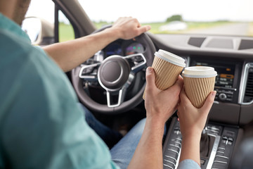 close up of couple driving in car with coffee cups