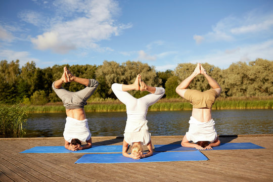 people making yoga headstand on mat outdoors