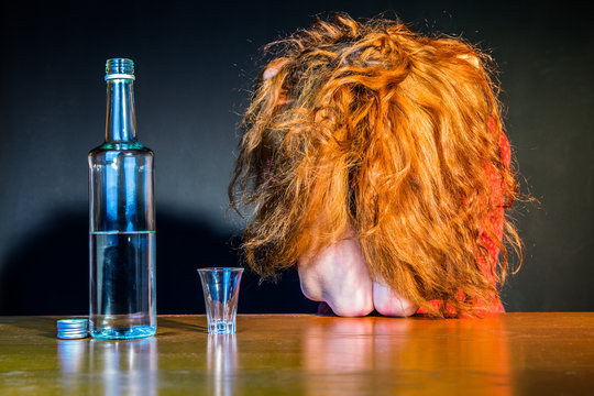 eine Frau sitzt einsam an einem Tisch mit einer Flasche Schnaps und einem Schnapsglas