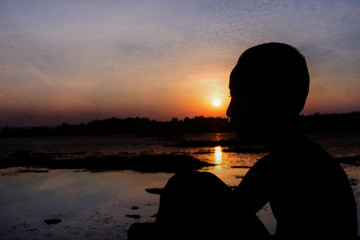 Fototapeta premium Silhouette of the boy sit hugged knees look the sunset.